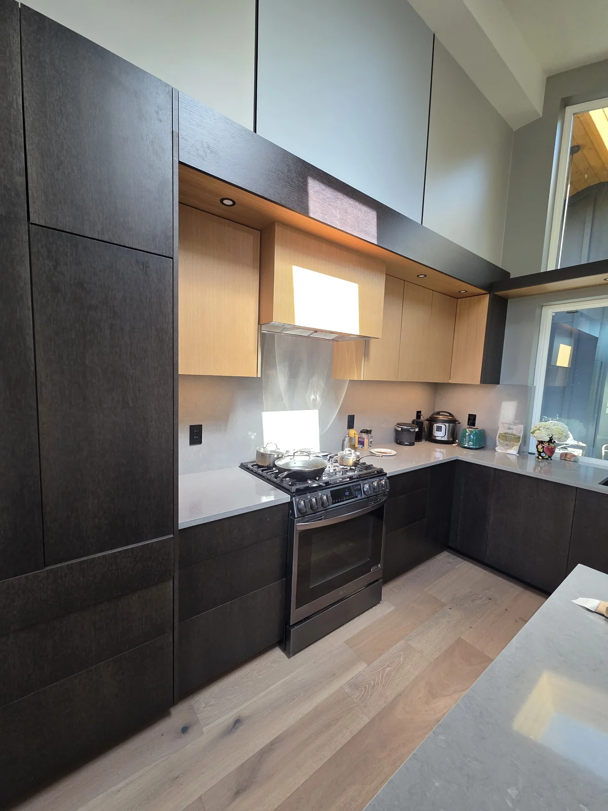 Modern kitchen remodel in Redmond, WA, with two-tone custom cabinetry, dark slab cabinets, warm wood uppers, quartz countertops, stainless-steel appliances, recessed lighting, and an open layout.